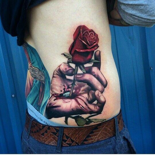 hand holding a rose bleeding tattoo design on side lower back